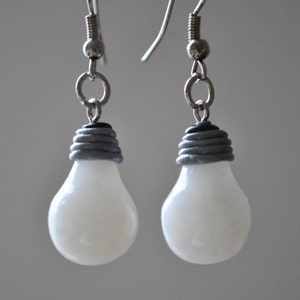 May include: A pair of silver lightbulb earrings with a grey and black base. The lightbulbs are white and opaque.