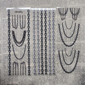 May include: A sheet of nail art stickers featuring various black and silver chain designs. The sheet includes multiple vertical chain strips and several draped chain patterns, all set against a background with printed text that reads CHAINS.