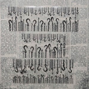 May include: A sheet of black nail art decals featuring various designs of metal chains and hooks arranged in rows. The background consists of repeating black text on a light gray surface. The text KHAOS KREATIONS is printed vertically.