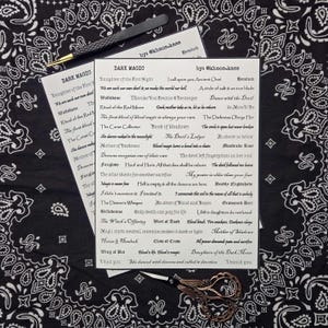 May include: Two white rectangular sticker sheets featuring black text titled DARK MAGIC by @khaos.kass. The sheets contain various phrases and words like Daughter of the First Night, Wolfsbane, and Book of Shadows, accompanied by a black tool and scissors.