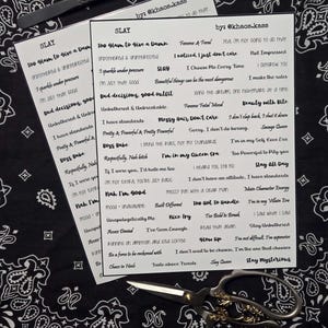 May include: Two sheets of white stickers with sassy phrases like "Slay" and "Too Glam to Give a Damn" are displayed. A pair of gold-handled scissors and tweezers rest on a black and white paisley bandana.