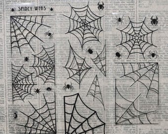 May include: A sheet of black spider web and spider decals on a background of vintage newspaper print. The text "SPIDEY WEBS" is printed in the upper left corner. The design features various web shapes and sizes with small spiders included.