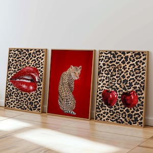 May include: Three framed art prints. One shows red lips, another a leopard on a red background, and the third depicts two cherries. The frames have a gold finish. The backgrounds of the lips and cherries are leopard print.