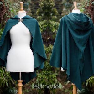 May include: A dark teal hooded cloak displayed on a mannequin. The cloak features a decorative clasp at the neckline and a flowing design. The cloak is made of a soft material and is displayed in front of a natural background.