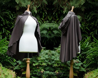May include: A brown hooded cape with a high collar and scalloped edges. The cape is displayed on a mannequin against a backdrop of green foliage.