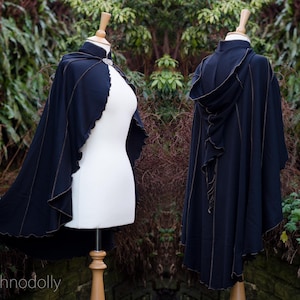 May include: A black hooded cape with a high collar and gold stitching. The cape is made of a soft, flowing fabric and has a relaxed fit.