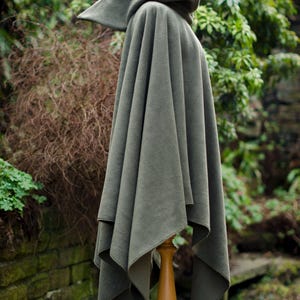 May include: A hooded cloak in a dark green color, made of a soft, plush fabric. The cloak is draped over a wooden stand and has a simple, elegant design.