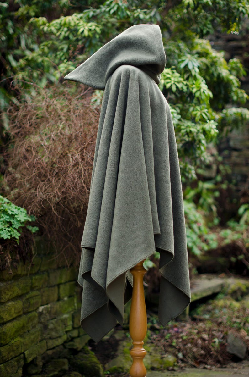 May include: A hooded cloak in a dark green color, made of a soft, plush fabric. The cloak is draped over a wooden stand and has a simple, elegant design.