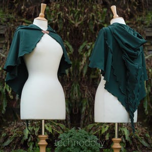 May include: A dark green hooded cape with a scalloped edge. The cape is displayed on a white mannequin.
