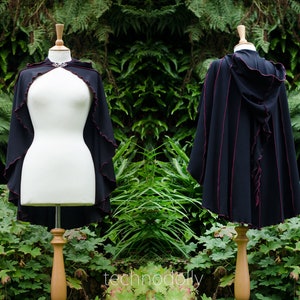 May include: A black hooded cape with a red trim and a ruffled edge. The cape is made of a soft, flowing fabric and is perfect for adding a touch of drama to any outfit.