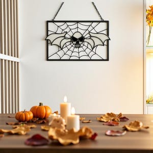May include: A black metal Halloween decoration with a skull and bat wings design within a spiderweb, suspended by a chain. The table is adorned with pumpkins, candles, and autumn leaves.