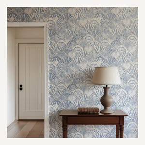 Pode incluir: Um quarto com papel de parede com padr&atilde;o de conchas em tons de azul e branco. Uma mesa de madeira castanha escura suporta uma l&acirc;mpada com um abajur bege e um livro. Uma porta branca e um ch&atilde;o de madeira tamb&eacute;m s&atilde;o vis&iacute;veis.