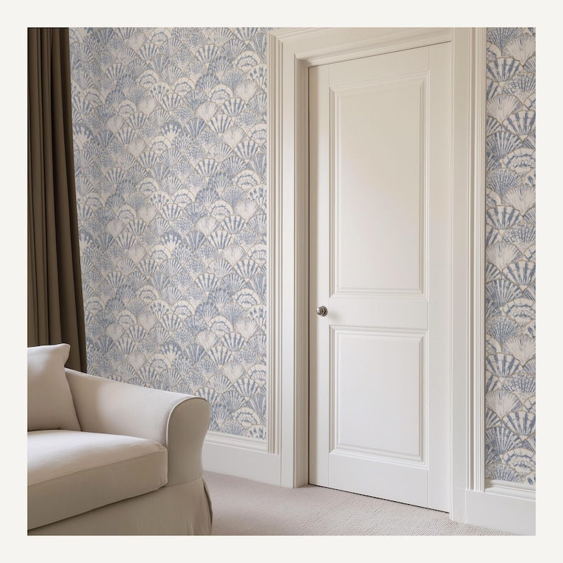 Pode incluir: Interior de uma sala com papel de parede com um padr&atilde;o repetitivo de conchas azuis e brancas. Uma porta e molduras brancas s&atilde;o vis&iacute;veis, juntamente com um sof&aacute; bege e uma cortina castanha. O papel de parede adiciona um tema costeiro.