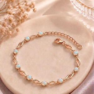 Puede incluir: Una pulsera en tono oro rosa que presenta una serie de pequeñas piedras redondas de color blanco opalescente iridiscente, engastadas en una delicada cadena de eslabones metálicos trenzados, con cierre de mosquetón y cadena extensora ajustable.