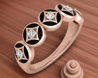 May include: Rose gold ring featuring a series of black circular accents, each with a central diamond. The ring's design includes a matching rose gold accent piece. The ring is displayed on a wooden surface.