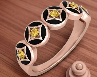 May include: A rose gold ring featuring a series of circular black and gold accents, each centered with a yellow gemstone. The ring's design includes a small, matching decorative element.
