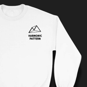Può includere: Felpa bianca girocollo con la scritta "HARMONIC PATTERN" e un logo di montagna geometrico nero. La felpa a maniche lunghe presenta un design minimalista.