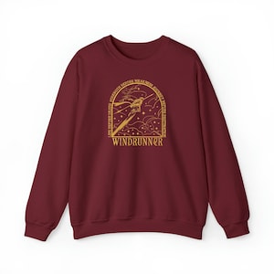May include: A maroon sweatshirt with a gold graphic design. The design features a stylized illustration with the text "LIFE BEFORE DEATH, STRENGTH BEFORE WEAKNESS, JOURNEY BEFORE DESTINATION" and the word "WINDRUNNER".