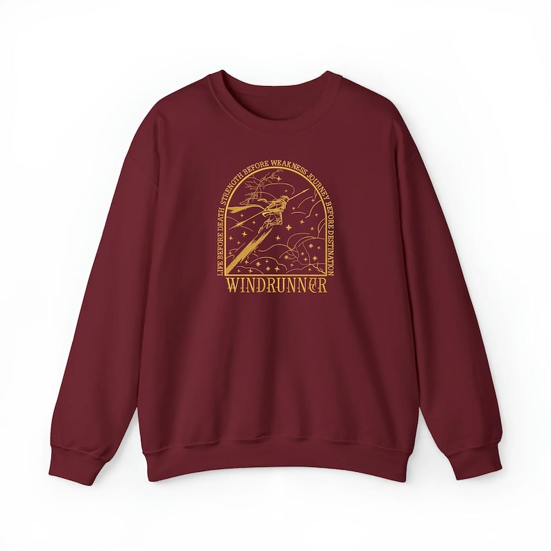 May include: A maroon sweatshirt with a gold graphic design. The design features a stylized illustration with the text "LIFE BEFORE DEATH, STRENGTH BEFORE WEAKNESS, JOURNEY BEFORE DESTINATION" and the word "WINDRUNNER".