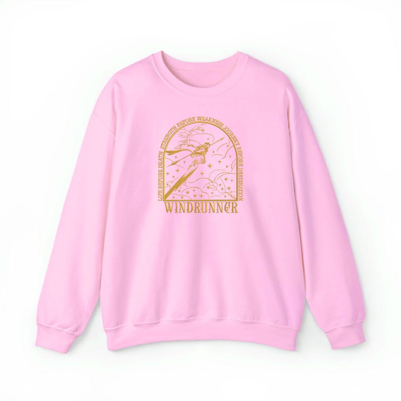 May include: A light pink sweatshirt with a gold graphic. The graphic features a stylized figure with the text "WINDRUNNER" at the bottom. The words "LIFE BEFORE DEATH, STRENGTH BEFORE WEAKNESS, JOURNEY BEFORE DESTINATION" are arched above the figure.