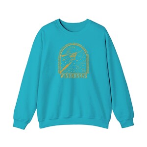 May include: A turquoise sweatshirt with long sleeves. The front features a gold illustration of a figure with a bow and arrow inside an arch, with the word "WINDRUNNER" below. The arch has text around the edges.