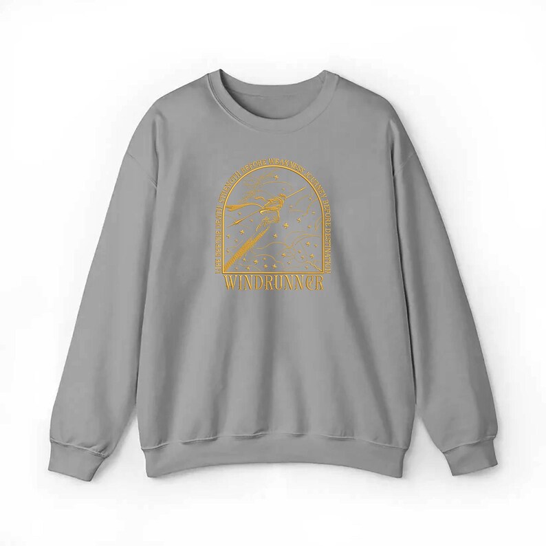 May include: A gray sweatshirt with a gold graphic design. The design features an arched frame with a stylized image of a person or object in flight, with the word "WINDRUNNER" below. The sweatshirt has a crew neck and long sleeves.