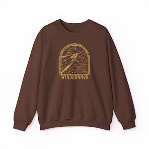 May include: A brown sweatshirt with a gold graphic featuring a stylized figure, sword, and text that reads "WINDRUNNER." The design is framed by the words "LIFE BEFORE DEATH, STRENGTH BEFORE WEAKNESS, JOURNEY BEFORE DESTINATION."