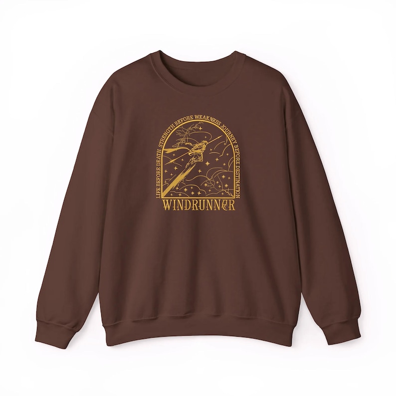 May include: A brown sweatshirt with a gold graphic featuring a stylized figure, sword, and text that reads "WINDRUNNER." The design is framed by the words "LIFE BEFORE DEATH, STRENGTH BEFORE WEAKNESS, JOURNEY BEFORE DESTINATION."
