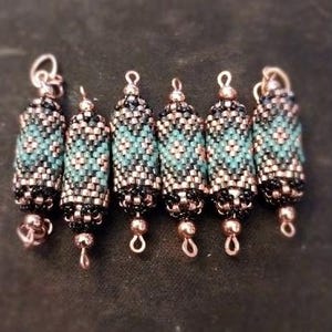 May include: Six beaded cylindrical pendants. Each pendant features a pattern of turquoise, black, and copper-coloured beads. The pendants have a loop at the top for hanging and a small bead at the bottom. The background is a dark, solid colour.