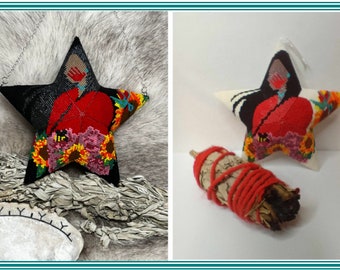 May include: A beaded star ornament with a red, black, and white design. The star is decorated with sunflowers and a bee. The ornament is hanging from a white string. A bundle of sage is also pictured.