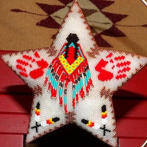 May include: A white star-shaped ornament with red handprints, a beaded Native American design in red, yellow, blue, and black, and a white background.