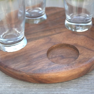 May include: A round wooden serving tray with three circular cutouts for glasses. The tray is made of dark brown wood and has a smooth, polished finish.