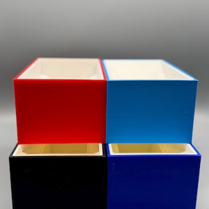 May include: Four small rectangular boxes stacked in two rows. The top row has a red box on the left and a blue box on the right. The bottom row has a black box on the left and a dark blue box on the right.