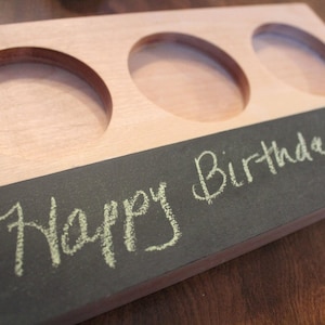 May include: Wooden serving tray with three circular cutouts. The tray has a light wood finish with a dark gray painted section at the bottom. The words "Happy Birthday!!!" are written in white chalk.