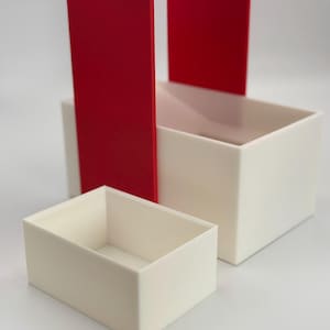 May include: A set of three nesting boxes, one red and two white. The red box is open on one side and the white boxes are closed.