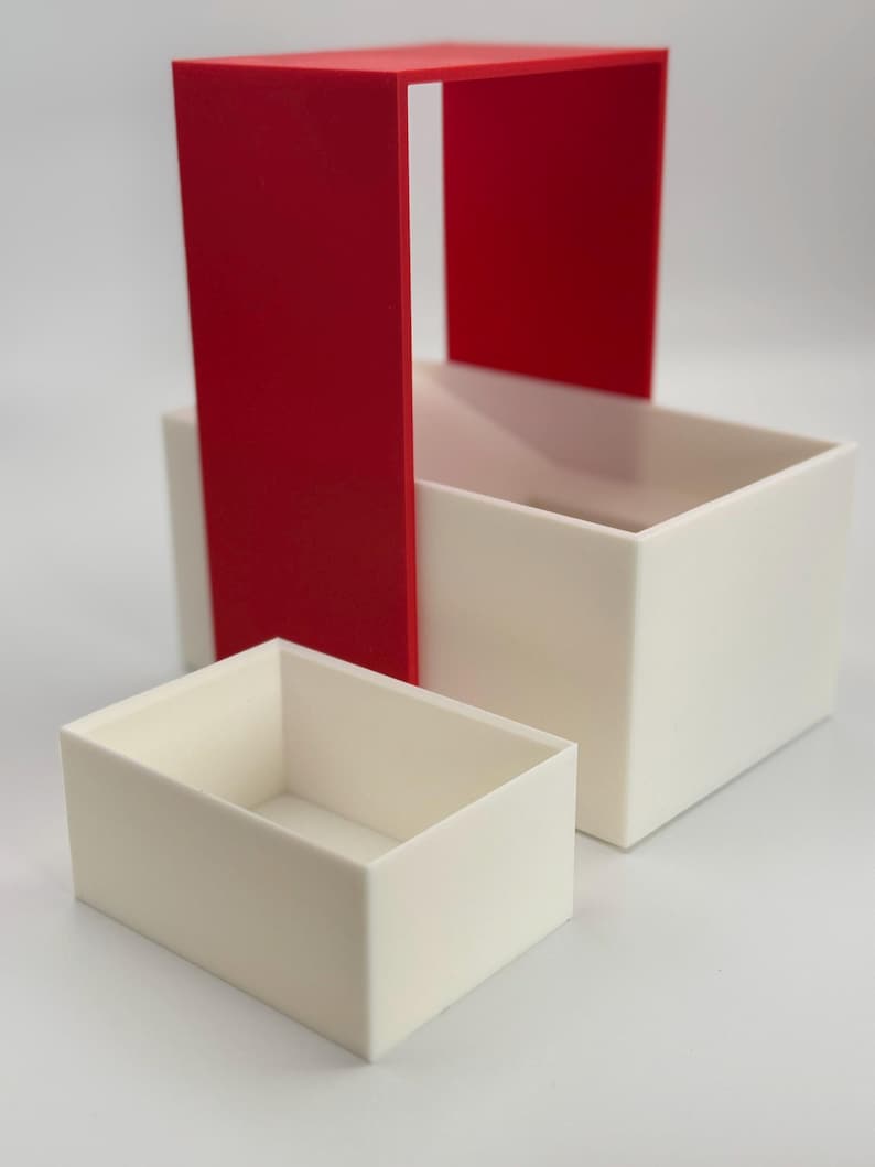 May include: A set of three nesting boxes, one red and two white. The red box is open on one side and the white boxes are closed.