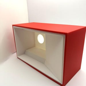 May include: A red box with a white interior and a circular opening. The box is made of a smooth, hard material and has a modern design.
