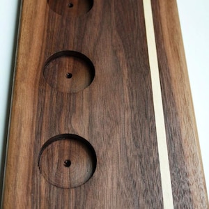 May include: A wooden serving tray with three circular cutouts and a thin white stripe down the center. The tray is made of dark brown wood.