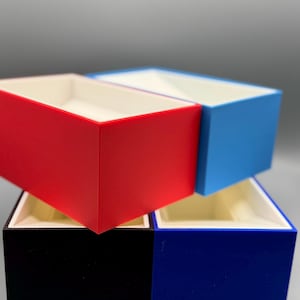 May include: Four empty boxes stacked on top of each other. The top box is light blue, the second box is red, the third box is black, and the bottom box is dark blue.