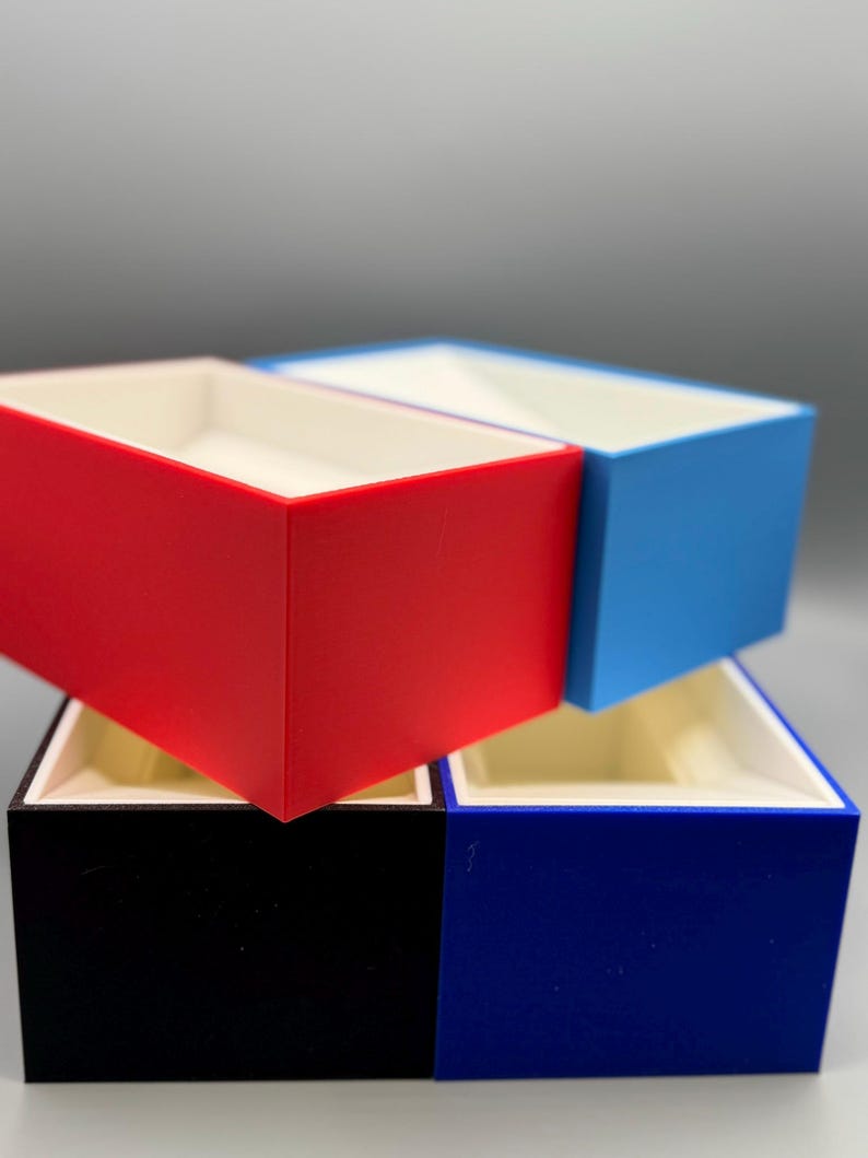 May include: Four empty boxes stacked on top of each other. The top box is light blue, the second box is red, the third box is black, and the bottom box is dark blue.