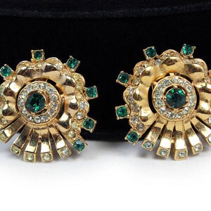 May include: A pair of gold tone earrings with a flower design. The earrings have green and clear rhinestones.