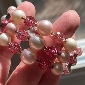 Può includere: Un braccialetto multifilo con perline rosa e bianche. Il braccialetto è realizzato con perline di cristallo rosa e perline di perla bianca.