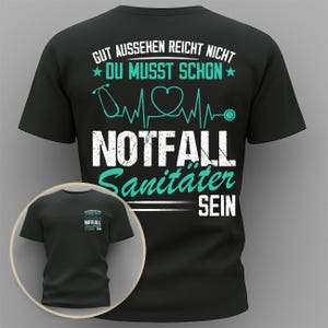 Op de afbeelding: Zwart t-shirt met de tekst "GUT AUSSEHEN REICHT NICHT DU MUSST SCHON" en "NOTFALL Sanitater SEIN" in wit en teal. Het ontwerp bevat een stethoscoop, hartslaglijn en een hartsymbool. Een kleinere afbeelding van het shirt staat linksonder.