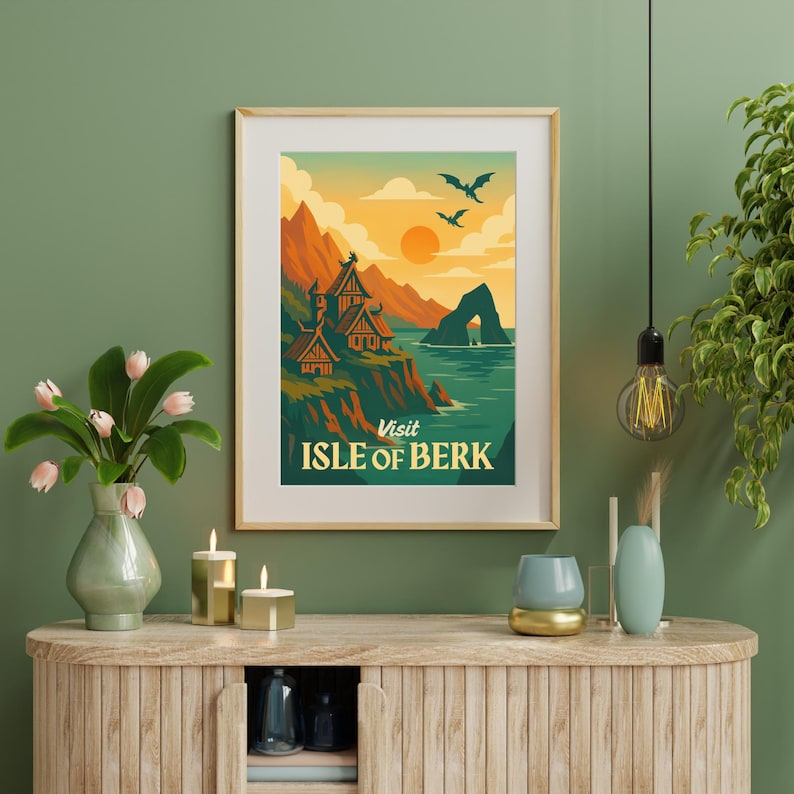 May include: A framed art print featuring a scenic landscape with the text "Visit Isle of Berk." The artwork depicts a coastal scene with mountains, buildings, and flying creatures, set against a sunset sky. The print is in a wooden frame.