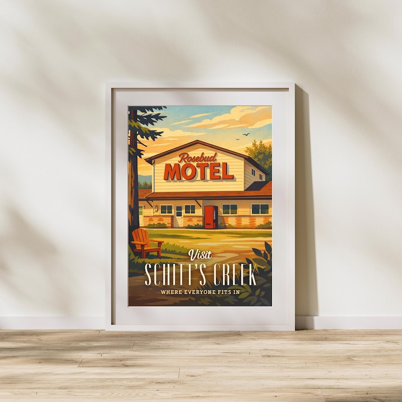 May include: Framed art print featuring a vintage-style illustration of the Rosebud Motel. The artwork showcases the motel's exterior with the text "Visit Schitt's Creek" and "Where Everyone Fits In". The color palette includes warm tones of orange, yellow, and brown.