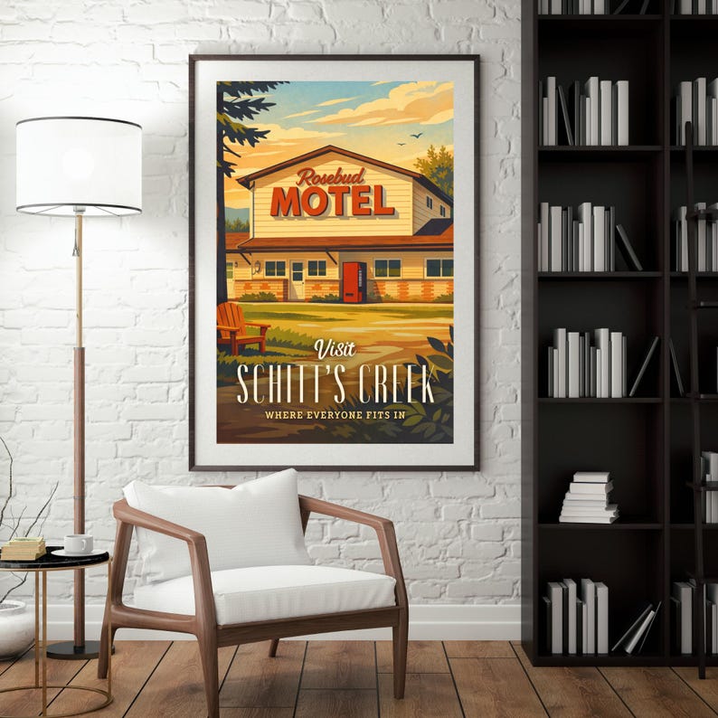 May include: A framed poster featuring the Rosebud Motel from Schitt's Creek. The artwork depicts the motel with a red door, set against a sunset sky. The text "Visit Schitt's Creek" is prominently displayed below the motel illustration.