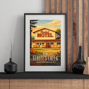 May include: Framed art print featuring a vintage-style illustration of the Rosebud Motel from Schitt's Creek. The artwork depicts the motel with a red door, a wooden chair, and the text "Visit Schitt's Creek". The sky is a gradient of blue and orange.