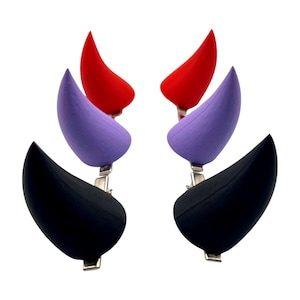 May include: Four pairs of costume horns in red, purple, and black. Each horn is attached to a silver-colored clip. The horns are arranged in pairs, with each pair consisting of a red, purple, and black horn.