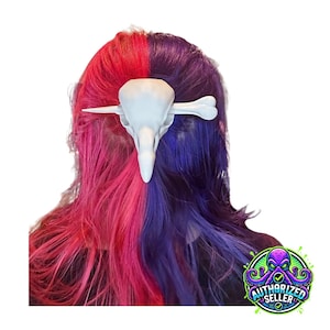 May include: A white bird skull hair clip is set against a backdrop of vibrant, split-dyed hair in shades of red and purple. The hair clip is a detailed replica of a bird skull, adding a gothic or alternative aesthetic. The image includes an "AUTHORIZED SELLER" logo.