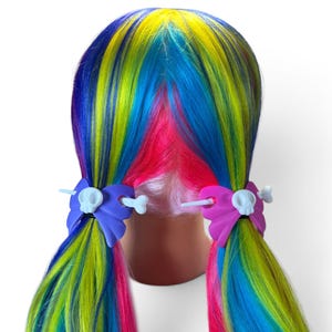 May include: A mannequin head with long, multi-colored rainbow hair styled in two pigtails. Each pigtail is secured with a purple or pink bow-shaped hair accessory featuring a white skull and crossbones design with a bone-shaped hair stick.